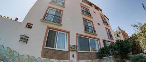 Un edificio de varios pisos con balcones, base de piedra y plantas en macetas.