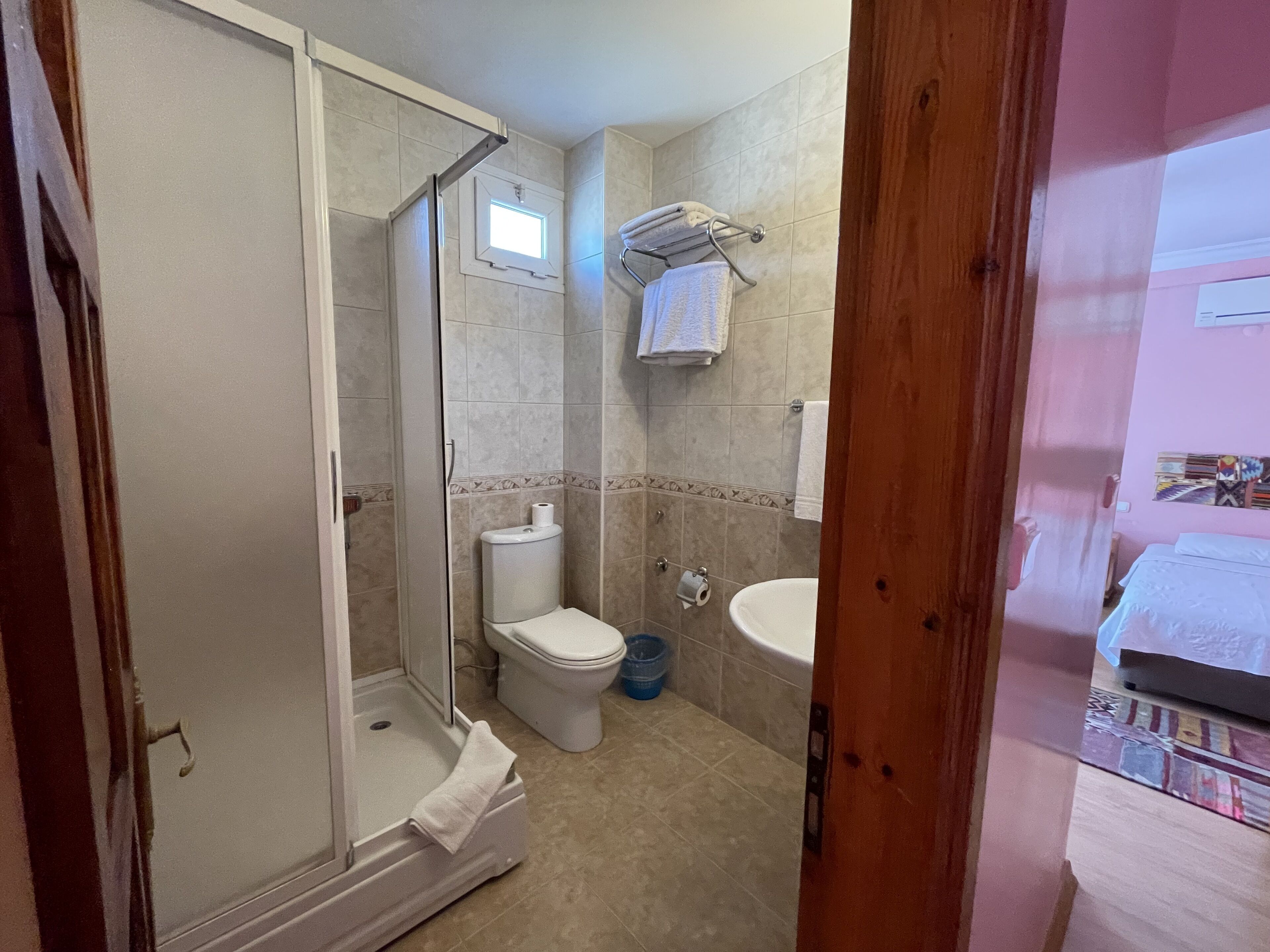 Une salle de bain équipée d’une douche, de toilettes et d’un lavabo, avec des murs carrelés et une porte en bois.