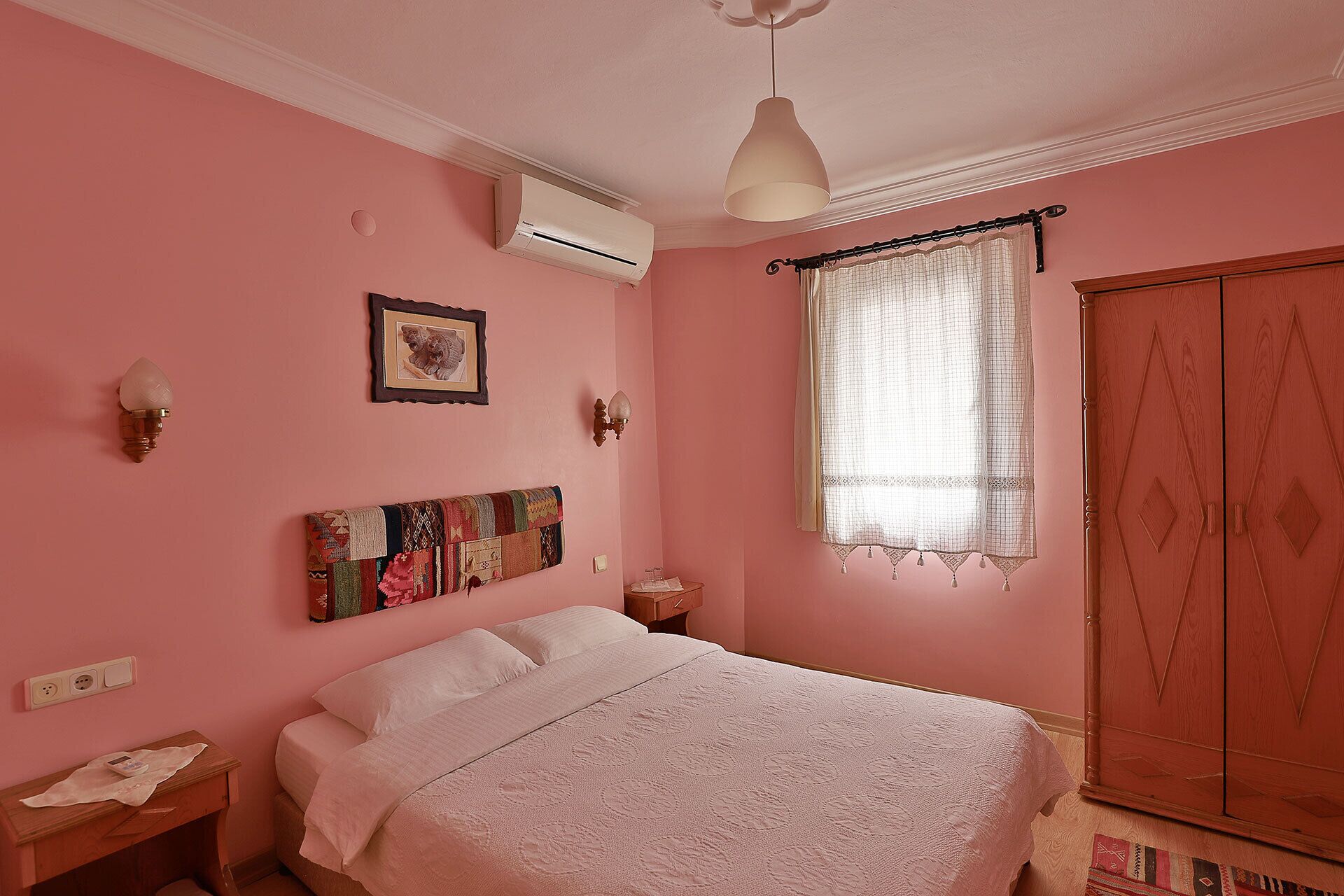 Une chambre à coucher comprenant un lit, une table de chevet, une lampe fixée au mur, une fenêtre avec des rideaux et une armoire.