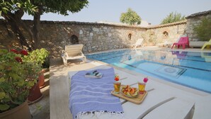A poolside area with lounge chairs, a stone wall, and potted plants. - Nazar Hotel (Selçuk)