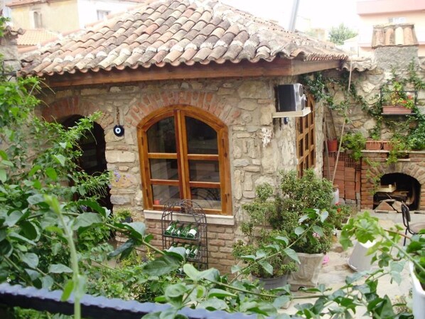 Un edificio de piedra con techo de tejas, un gran ventanal de arco y una chimenea de ladrillo.