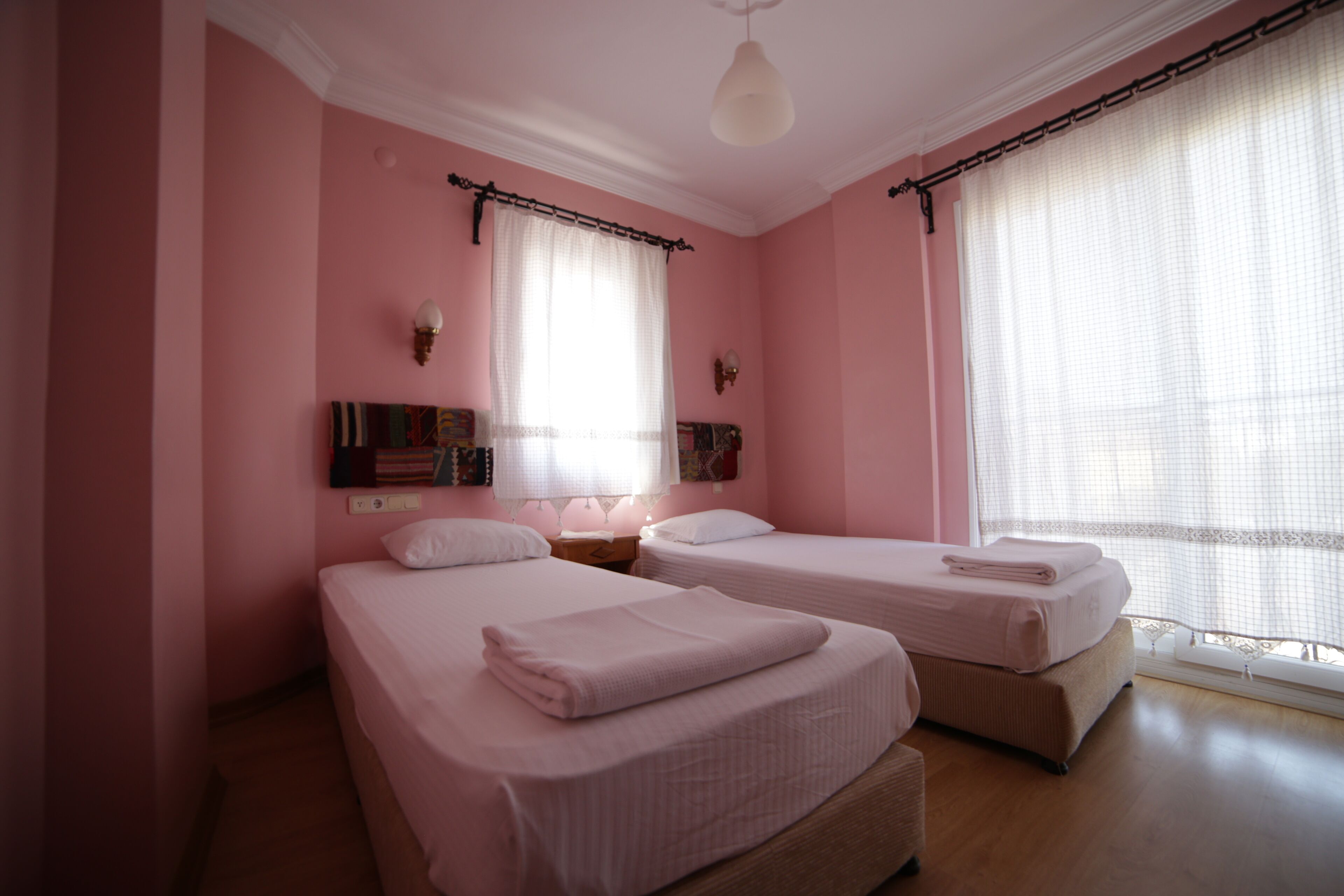 A room with two beds, pink walls, and a large window with sheer curtains.