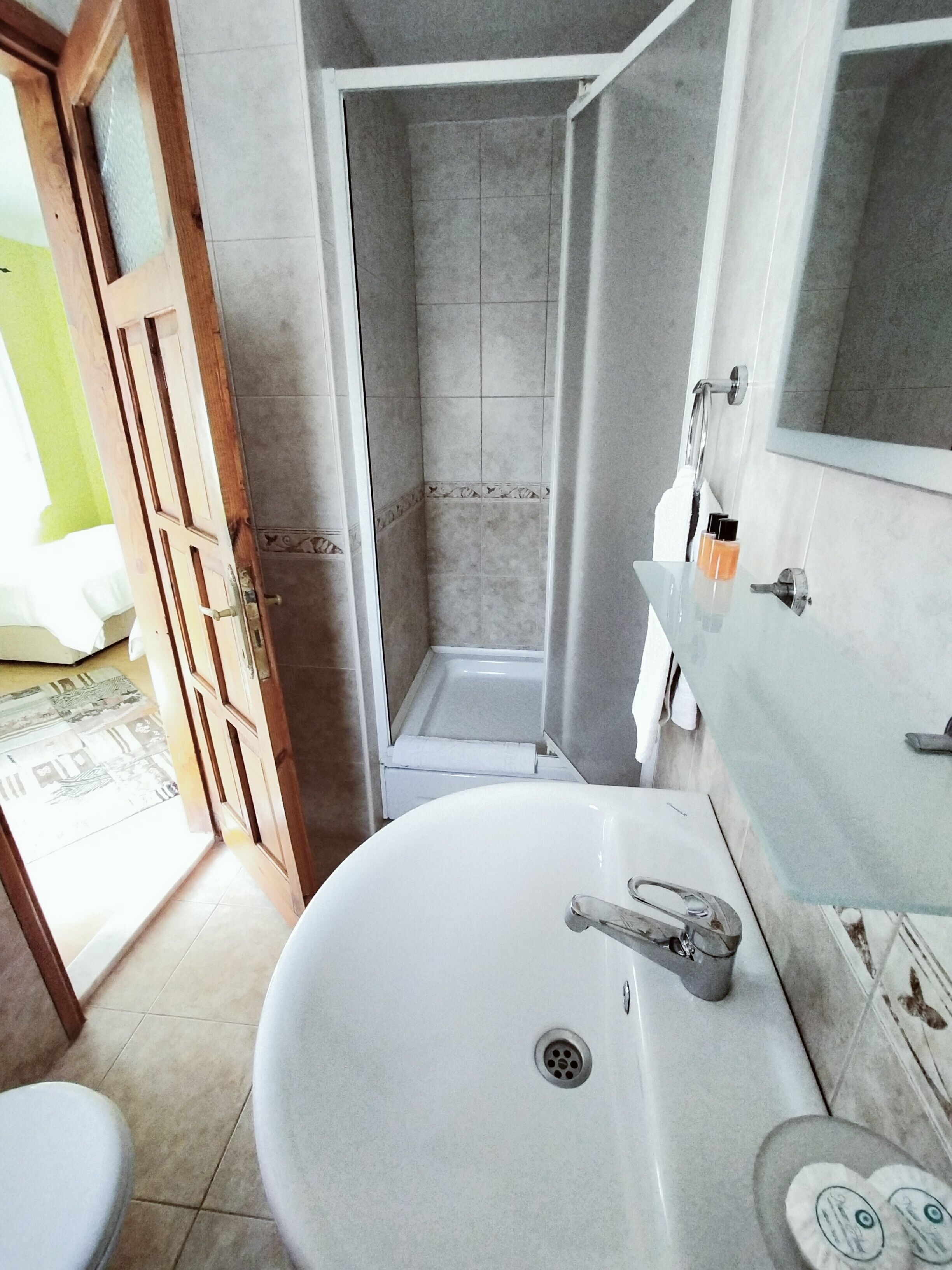 A bathroom with a white sink, a shower, and a wooden door.