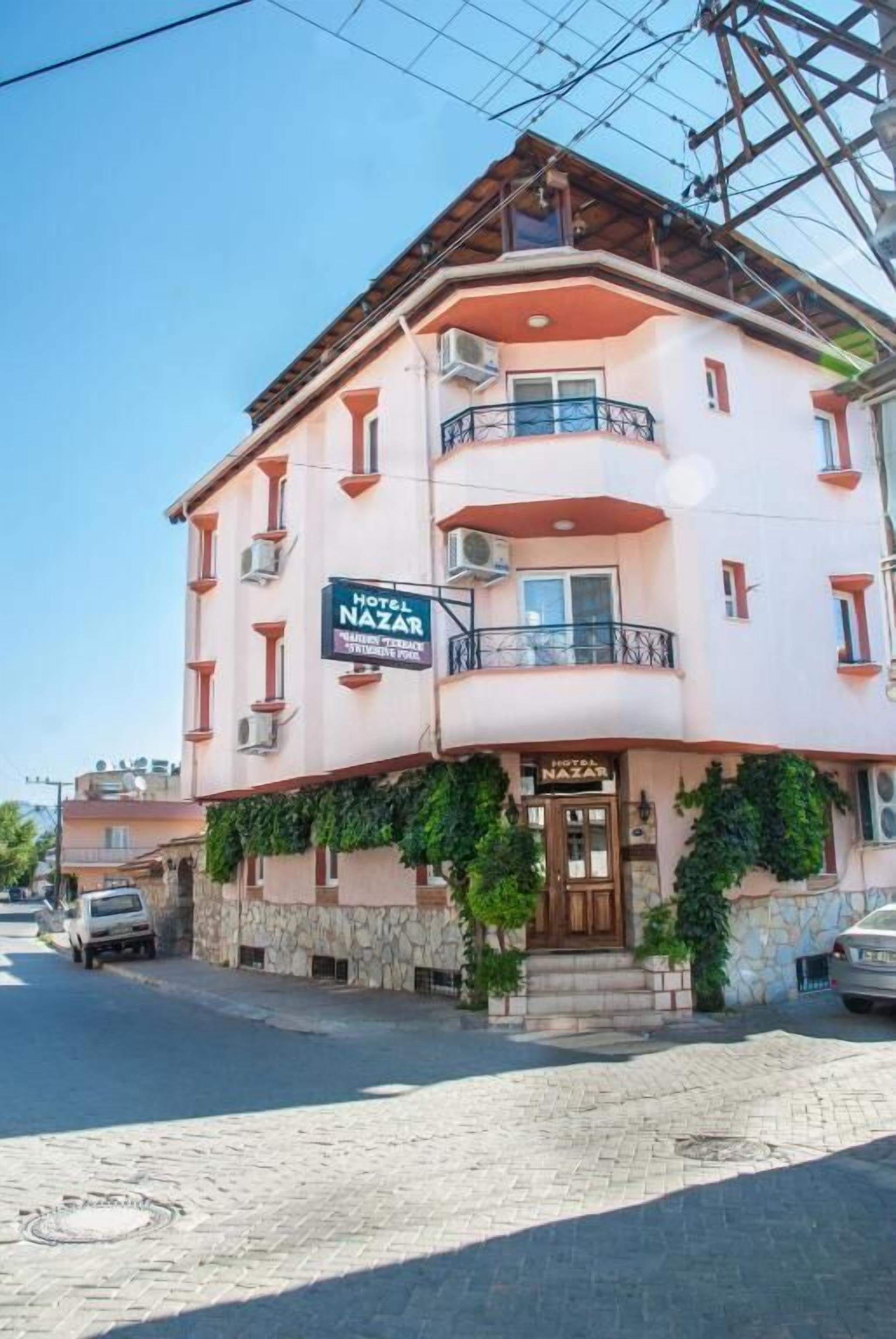A two-story hotel with a sign reading "Hotel Nazar." It features a stone facade, balconies, and a paved entrance area.