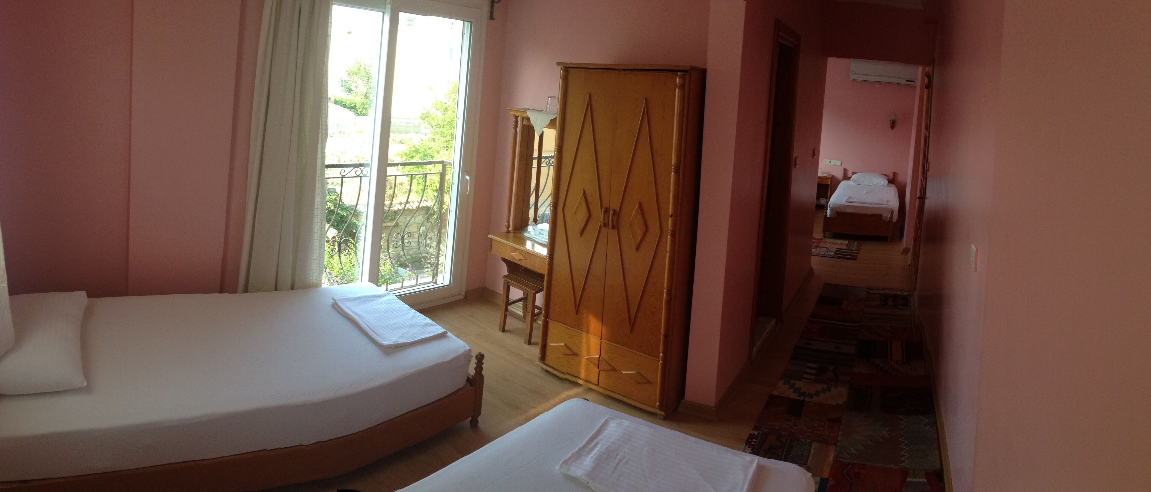 A bedroom with a bed, a wardrobe, a desk, and a window with a view of greenery.