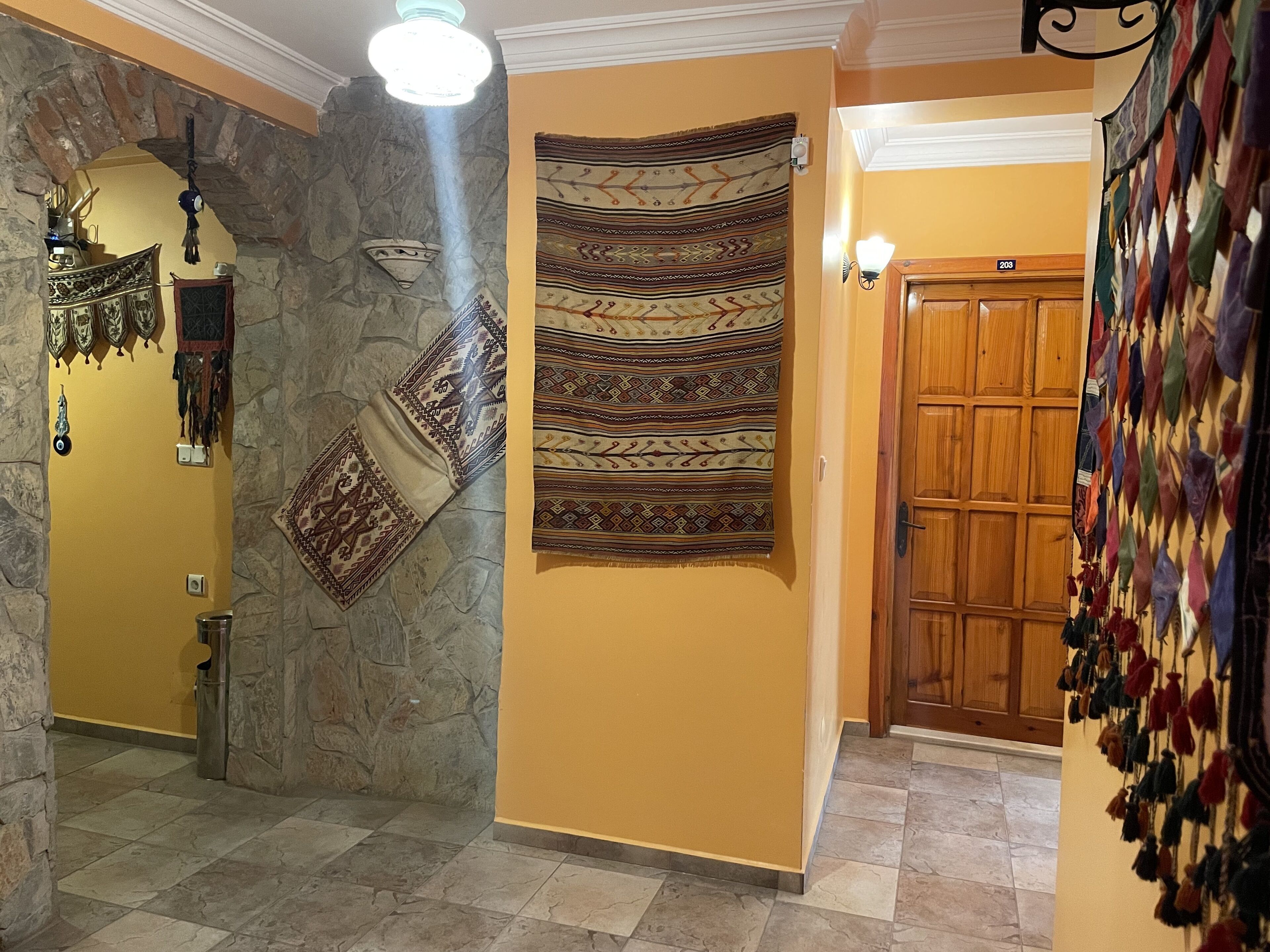 Un couloir avec un mur en pierre, une porte en bois et une décoration murale aux motifs géométriques.