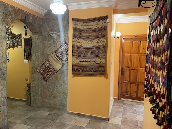Un pasillo con pared de piedra, puerta de madera y un tapiz con diseños geométricos.