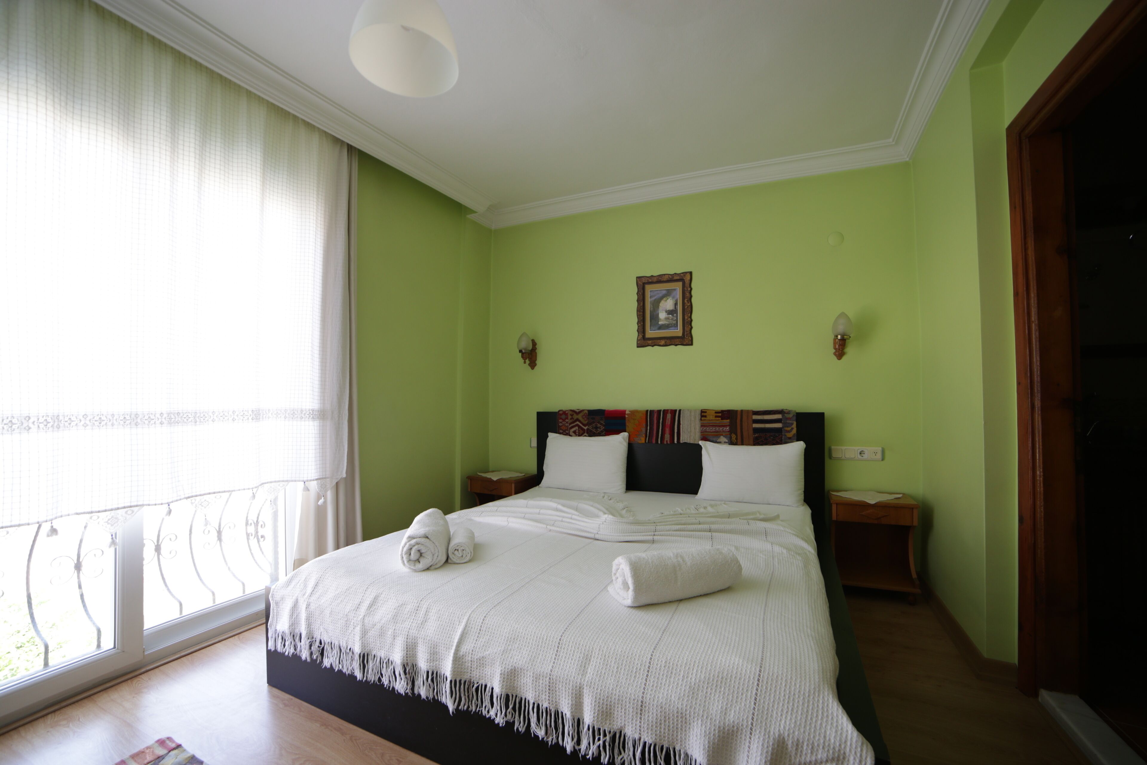 A neatly made bed with white linens, a headboard with a colorful pattern, and a framed picture on the wall.