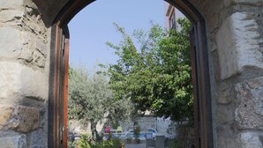 An arched stone doorway leading to a courtyard with a paved path, surrounded by stone walls and greenery. - Nazar Hotel (Selçuk)