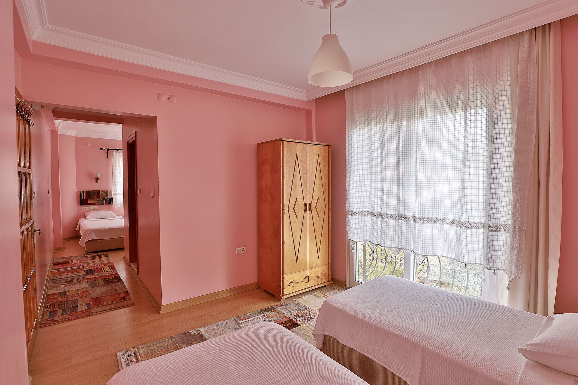 Une chambre à coucher décorée dans des tons de rose, avec deux lits, une armoire et une vue sur un balcon.