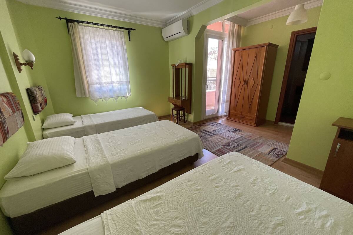 A room with two beds, a window with curtains, a wooden wardrobe, and a door leading to an outdoor area.