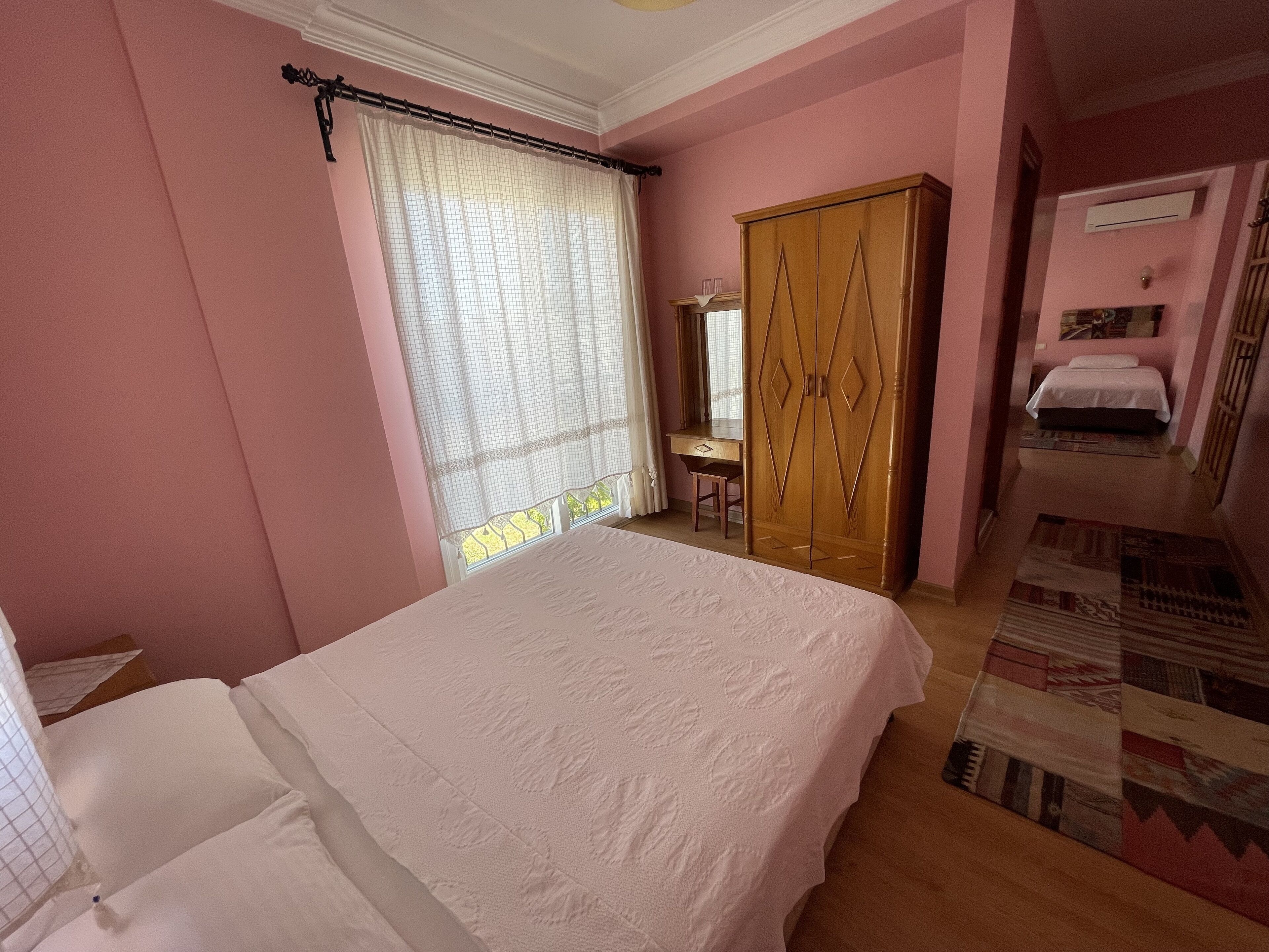 Un dormitorio con cama, armario, escritorio y ventana con cortinas.