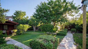A stone pathway leading through a well-maintained garden with various shrubs and trees. - HAYITBÜKÜ AHŞAPEVLERİ (Datça)