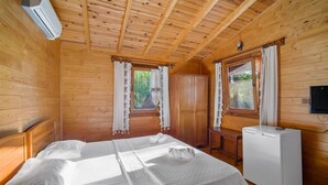 A wooden cabin room with a bed, a small table, a TV, and a window with curtains. - HAYITBÜKÜ AHŞAPEVLERİ (Datça)