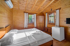 A wooden cabin room with a bed, a small table, a TV, and a window with curtains.