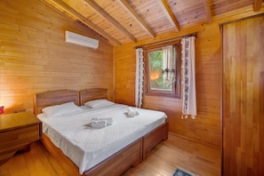 A wooden-paneled room with a bed, a nightstand, a window with curtains, and an air conditioning unit.