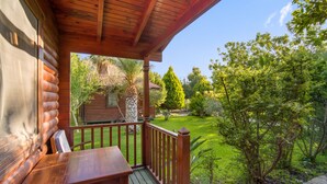 A wooden deck with a table and chairs, overlooking a lush garden and a small cabin. - HAYITBÜKÜ AHŞAPEVLERİ (Datça)