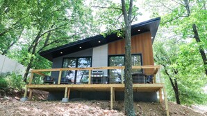 A modern house with a wooden deck, large windows, and a stone foundation. - Lakeside Modern Luxury Cabin with Lake View (Grove)