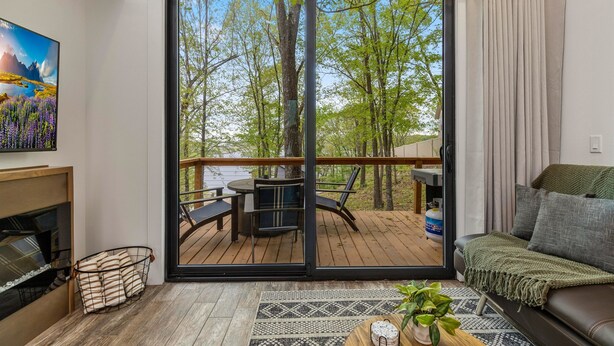 A living room with a sliding glass door to an outdoor deck, a fireplace, and a sofa with a throw blanket. - Lakeside Modern Luxury Cabin with Lake View (Grove)