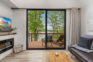 A modern living room with a sliding glass door leading to a deck, a sofa, a coffee table, and a fireplace.