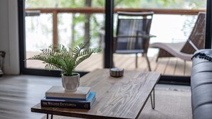 Una sala de estar moderna con una mesa de centro de madera, un helecho en maceta y una pila de libros.