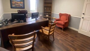 Une pièce comprenant un bureau, deux chaises, un fauteuil rouge, une bibliothèque et un tableau accroché au mur.