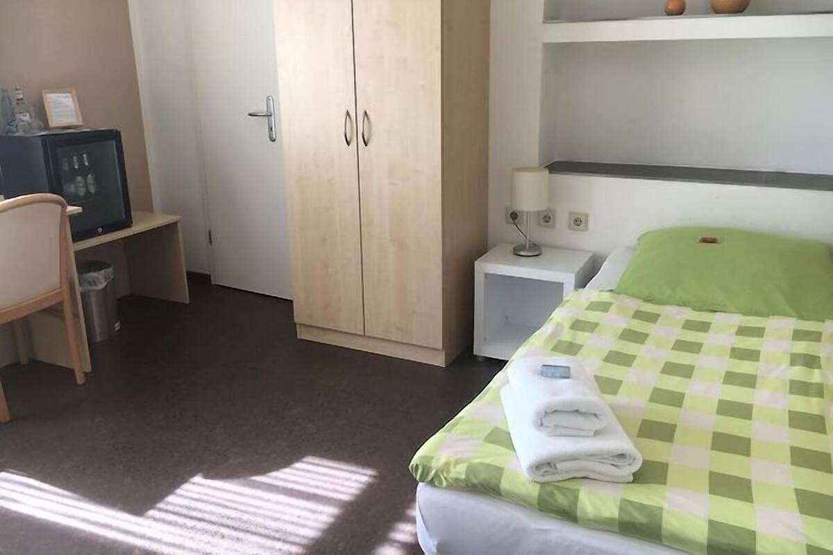 A hotel room with a bed, a desk, a wardrobe, and a nightstand.