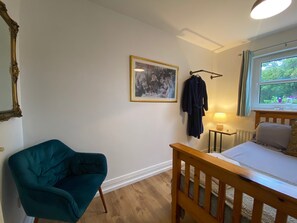 A bedroom with a bed, a chair, a bedside table with a lamp, a window with a view, and a framed picture on the wall. - The Yellow Door Cottage (Moville)