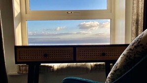 A room with a desk and a chair, a window with a view of the sky and clouds, and a patterned cushion on the chair. - The Yellow Door Cottage (Moville)