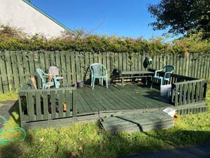 A wooden deck with outdoor furniture, including a table and chairs, surrounded by a wooden fence and greenery. - The Yellow Door Cottage (Moville)