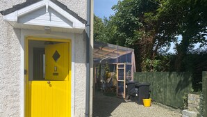 A yellow door with a small window, a metal gate, and a gravel driveway. - The Yellow Door Cottage (Moville)
