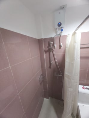 A small bathroom with a shower, a white toilet, and a wall-mounted heater. - Nest Suites (Quezon City)