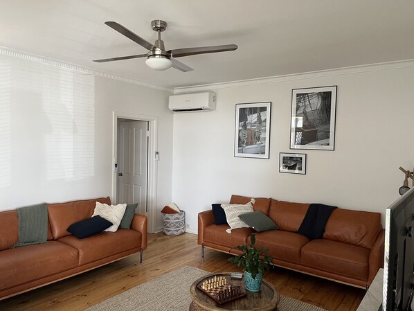 A living room with two brown leather sofas, a ceiling fan, and a coffee table with a chess set and a plant. - Absolute Beachfront - simply enjoy  (Henley Beach)