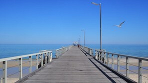 A wooden pier extending into the sea with railings on both sides and a clear sky above. - Absolute Beachfront - simply enjoy  (Henley Beach)