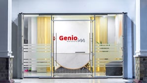 Entrada de um hotel moderno com fachada de vidro, logotipo Genio central e piso de mármore.
