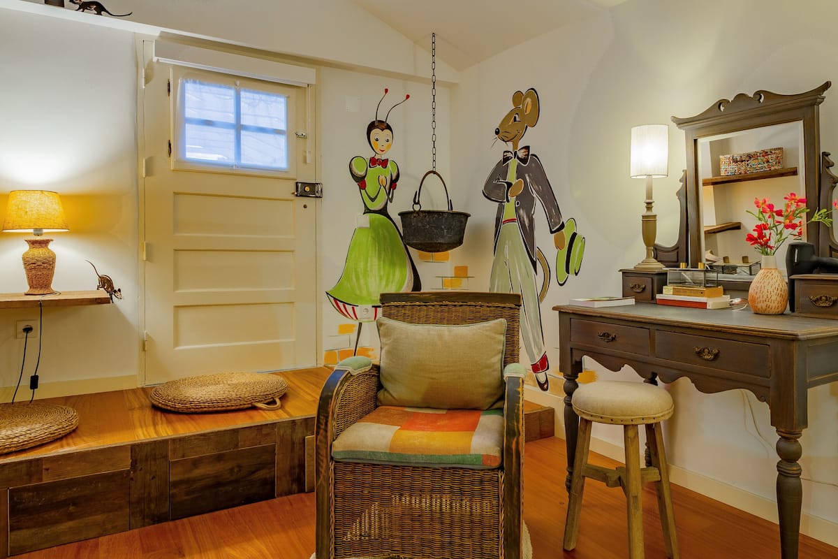 A room with a wicker chair, a wooden desk, a mirror, and a hanging basket.