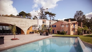 A swimming pool with a patio area, a building with a balcony, and a garden with trees and plants. - Villa Cerrado das Fontainhas (Sintra)
