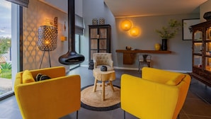 A modern living room with a fireplace, yellow chairs, a round wooden table, and a bookshelf. - Villa Cerrado das Fontainhas (Sintra)
