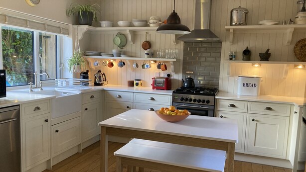 Een moderne keuken met witte kasten, een houten eettafel en diverse keukenapparaten.