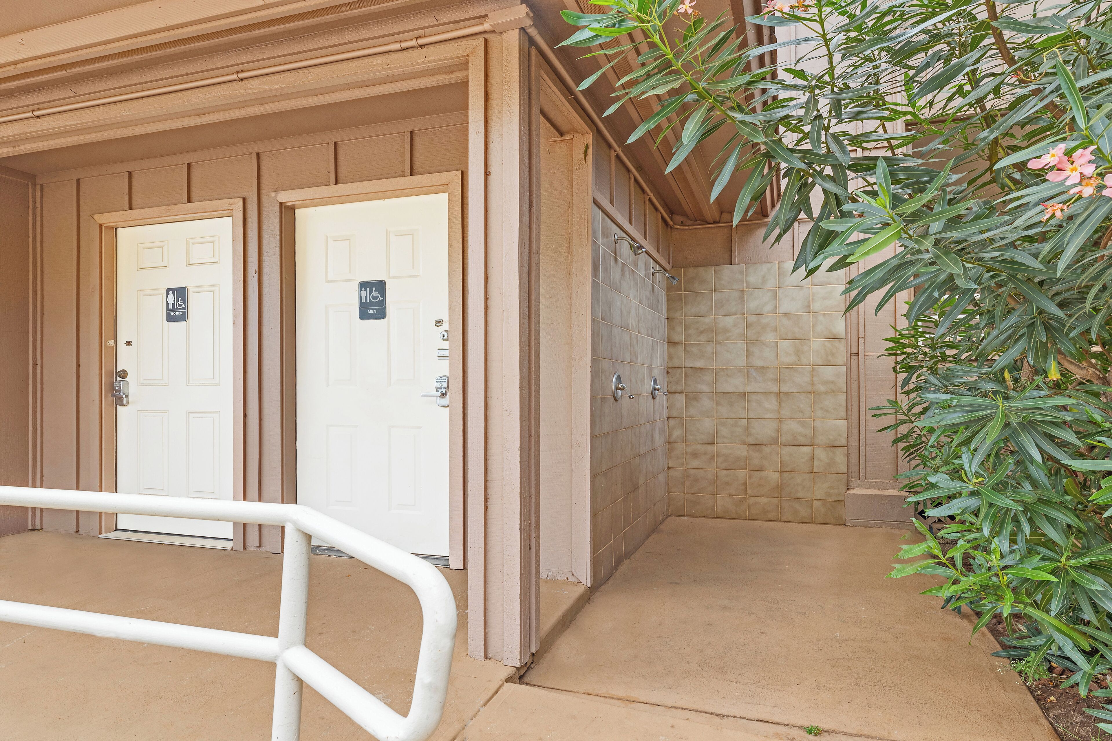 Entrada de edificio con dos puertas, una señalizada para hombres y otra para mujeres, y un área cubierta con pared de azulejos.