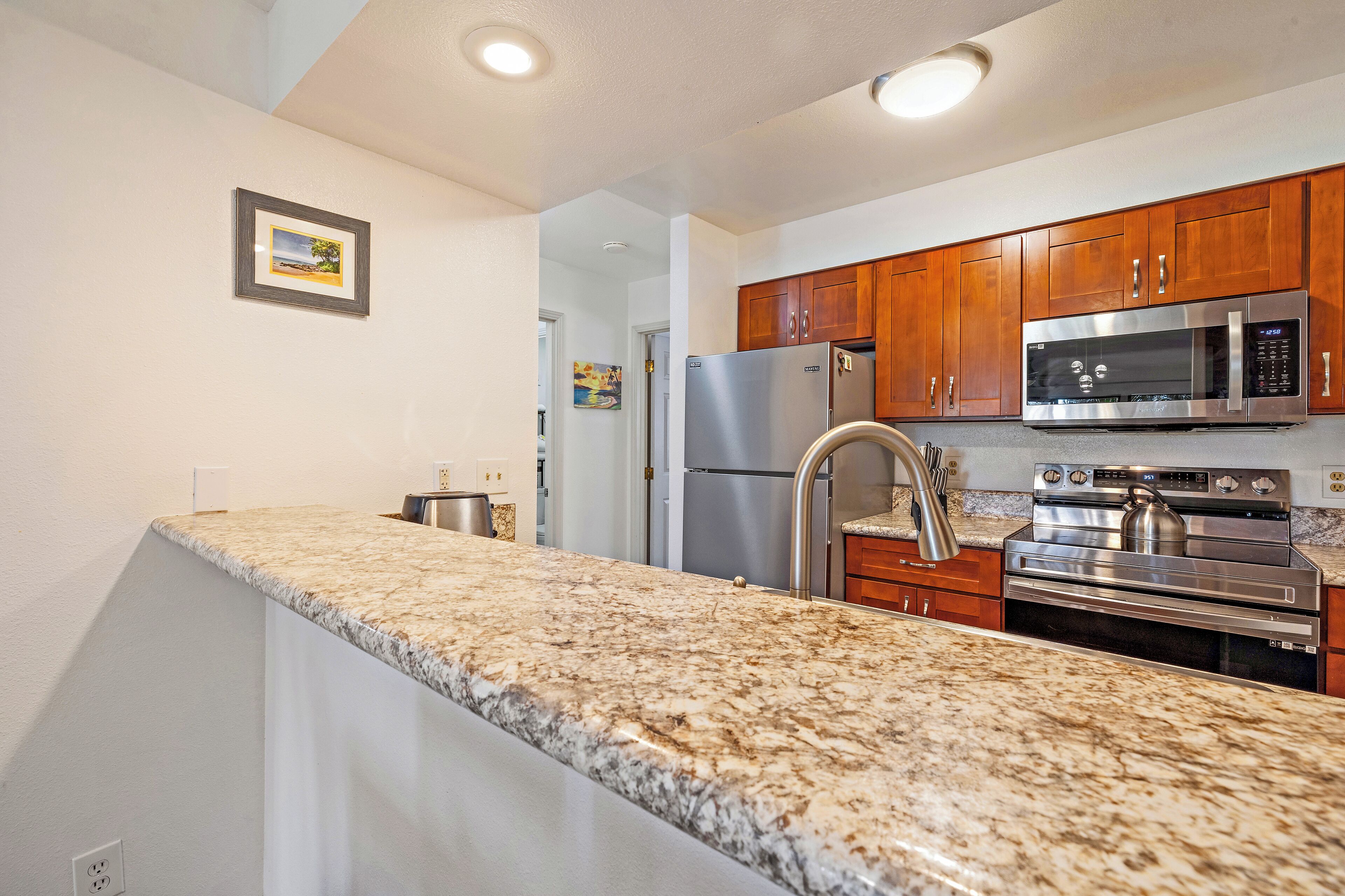 A kitchen with granite countertops, stainless steel appliances, wooden cabinets, and recessed ceiling lights.