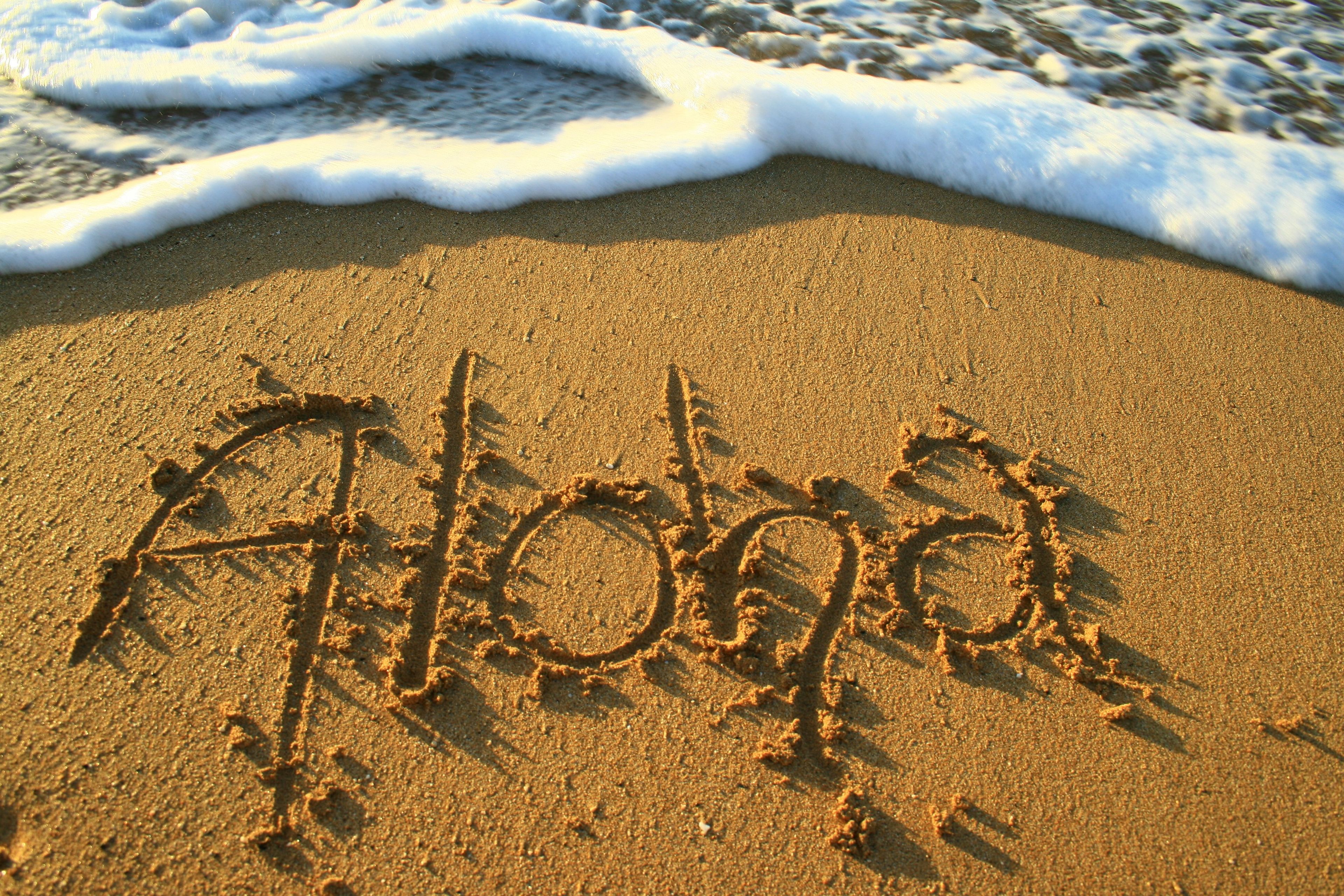 Een zandstrand met de tekst 'Aloha' in het zand geschreven.