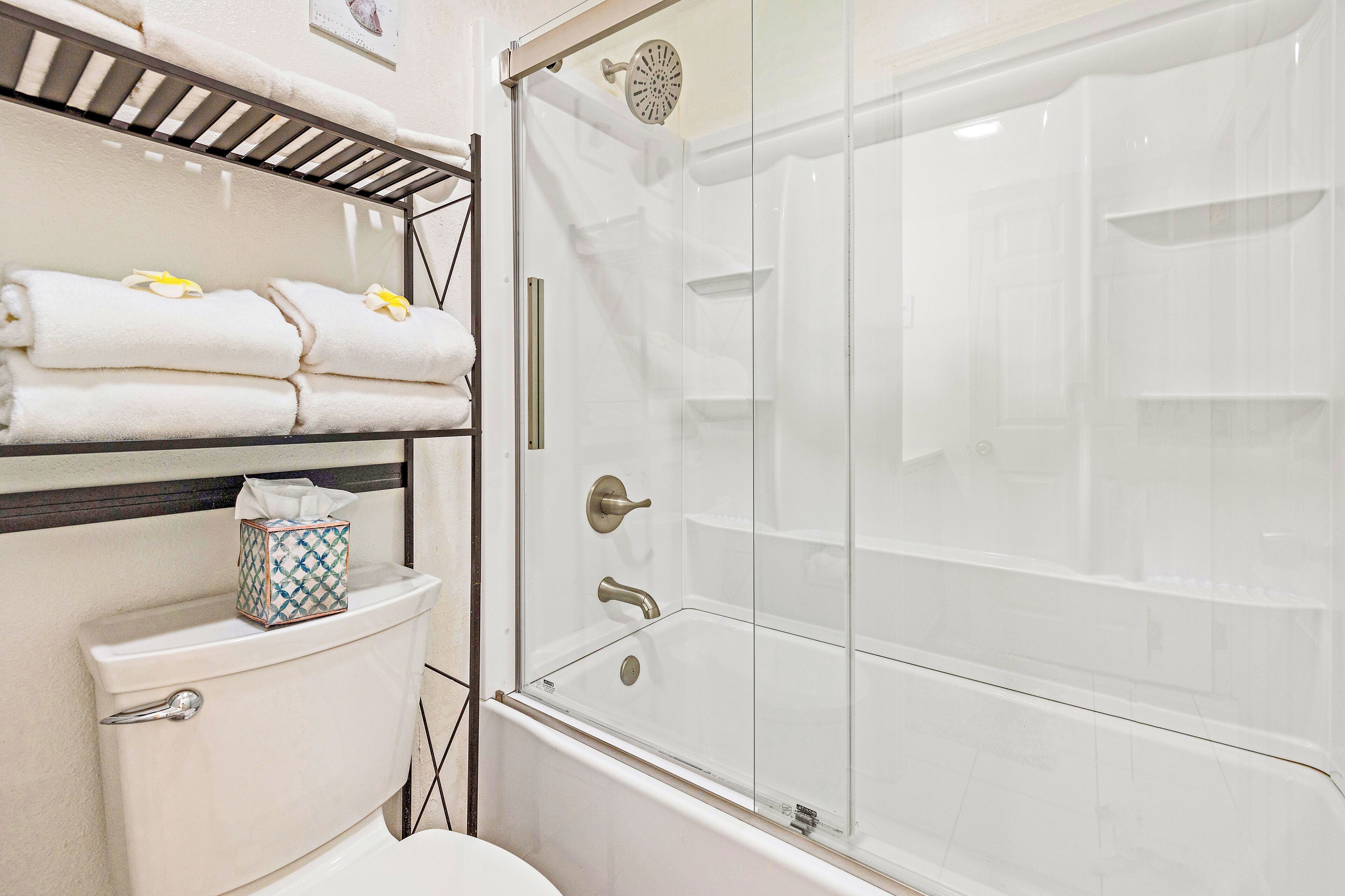 A bathroom with a glass-enclosed shower, a toilet, and a shelf with folded towels.