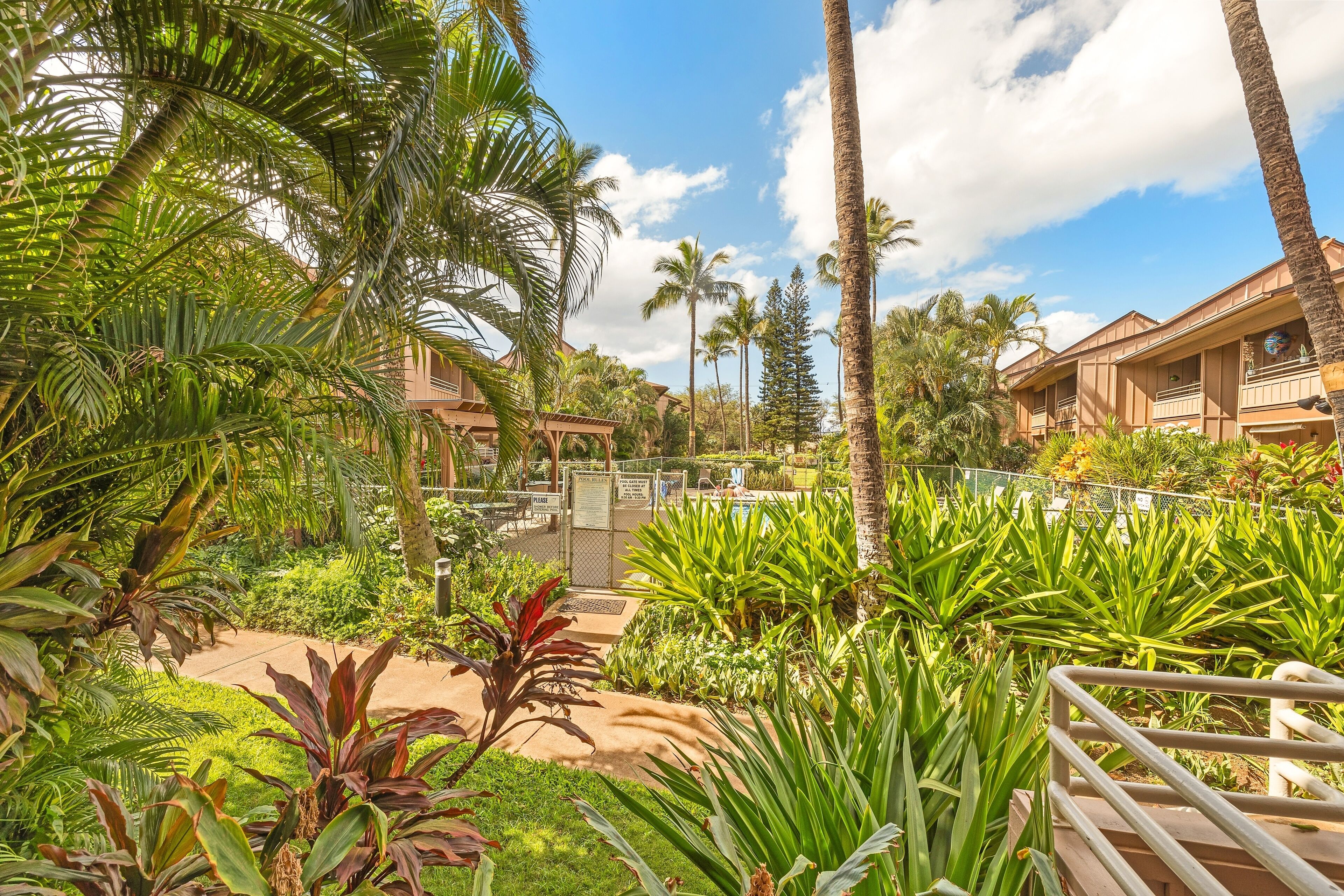 A resort with multiple buildings, lush tropical vegetation, and a fenced area with a pathway.
