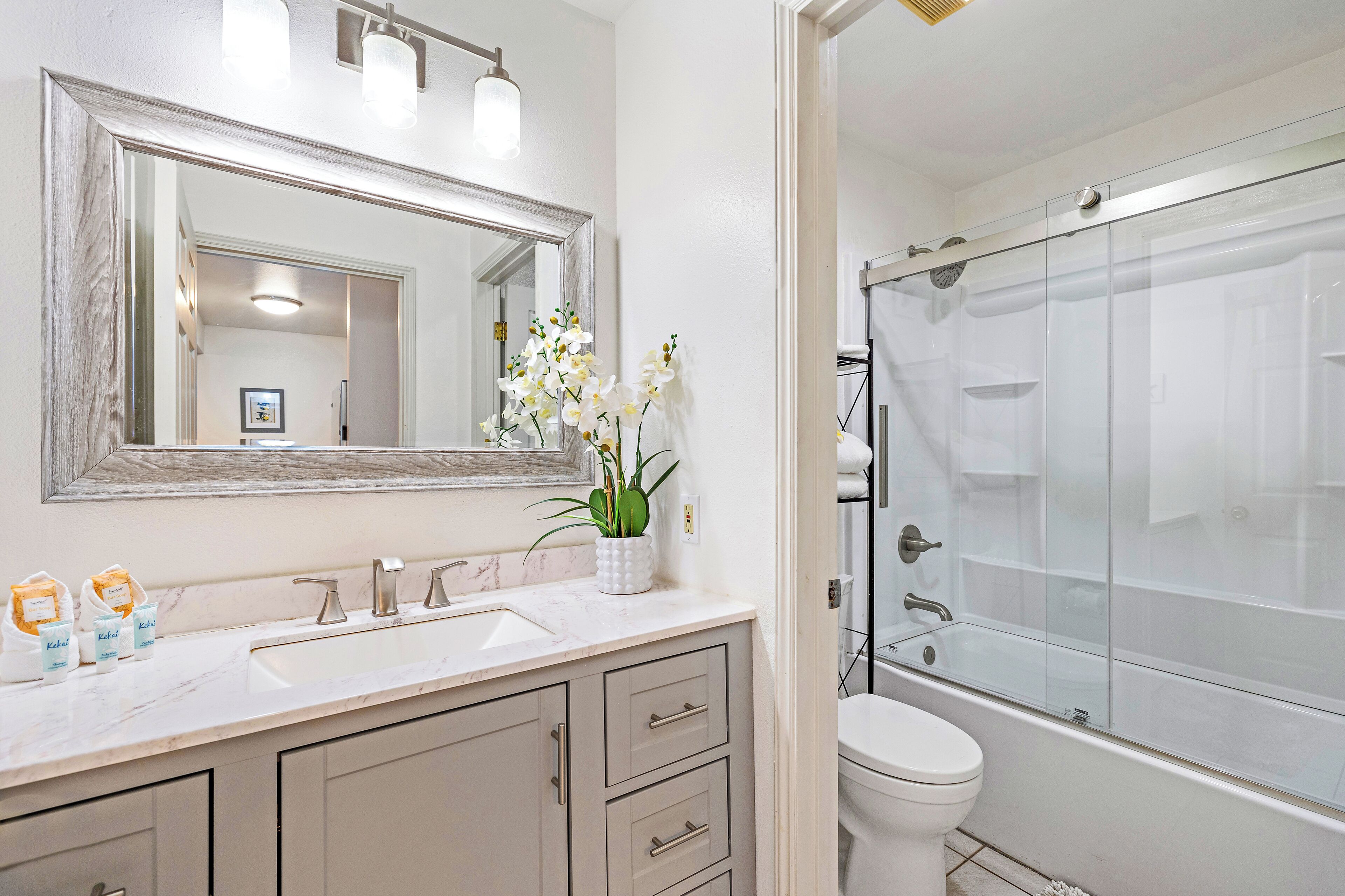 Une salle de bain avec un grand miroir, un lavabo, des toilettes et une douche à parois de verre.