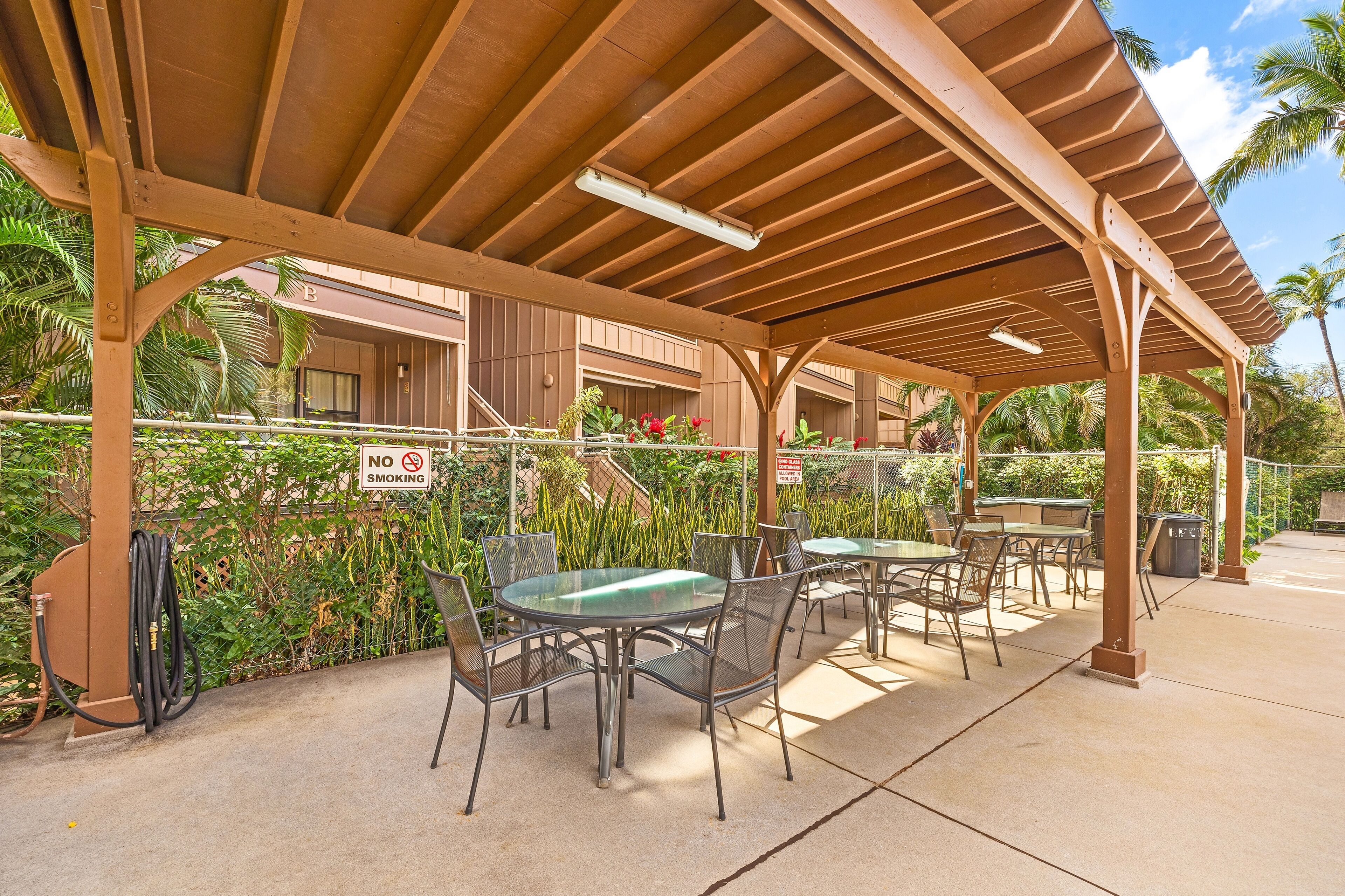 An outdoor covered patio with tables and chairs, a 'No Smoking' sign, and a view of a building with balconies.