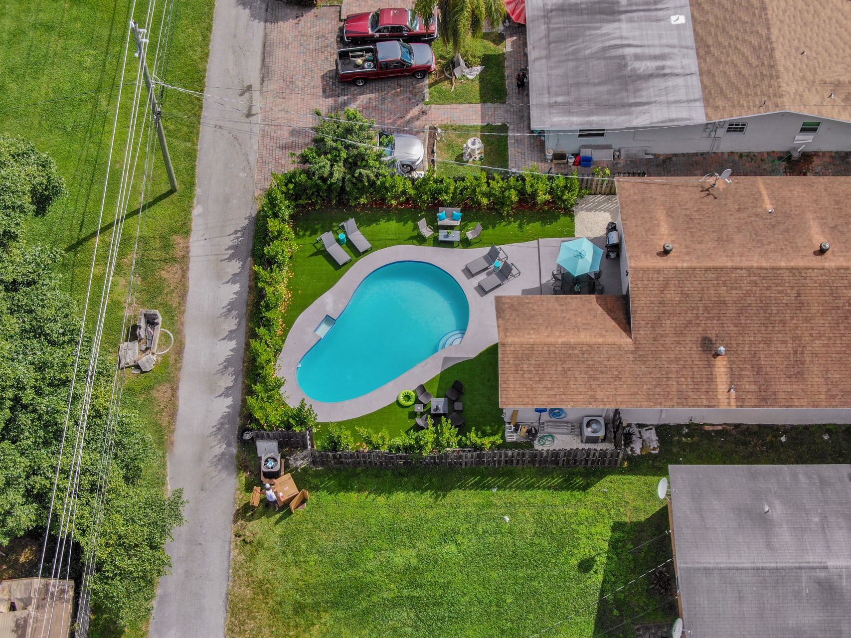 Vista aérea de um bairro residencial com piscina, casas vizinhas e um quintal cercado.