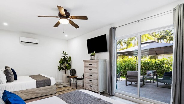 A modern bedroom with a bed, a dresser, a ceiling fan, a TV, and a sliding glass door leading to an outdoor patio. - Private Heated Pool & Lovely Home (Dania Beach)