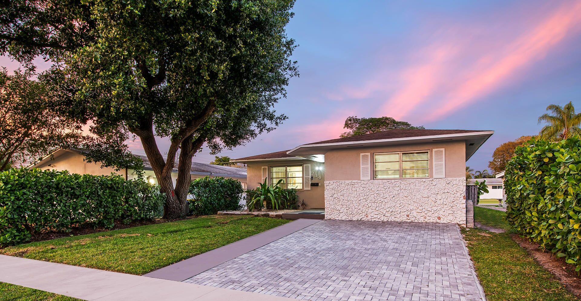 A modern two-story house with a stone facade, a paved driveway, and a large tree in the front yard.