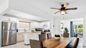 A modern kitchen with white cabinets, stainless steel appliances, and a wooden dining table with chairs. - Private Heated Pool & Lovely Home (Dania Beach)